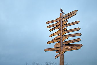 Wooden signpost with multiple directional arrows against blue sky