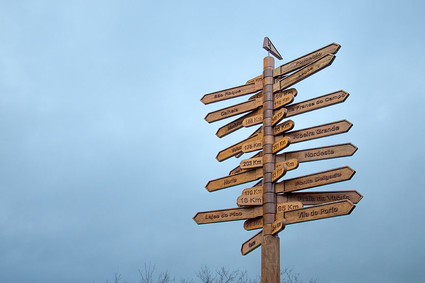 Wooden signpost with multiple directional arrows against blue sky