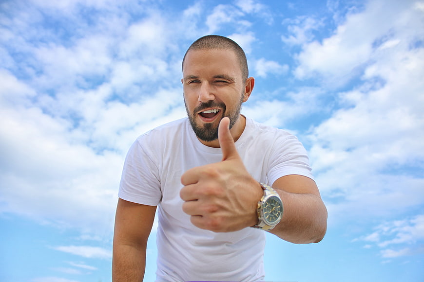 Happy man giving thumbs up against blue sky