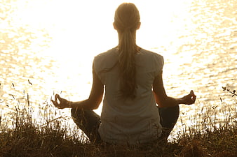 Woman meditating by water at sunset