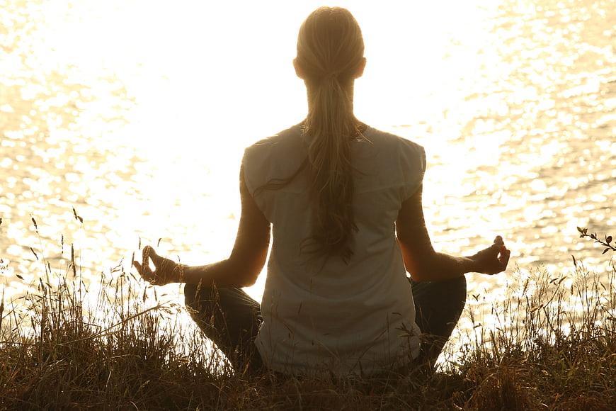 Woman meditating by water at sunset