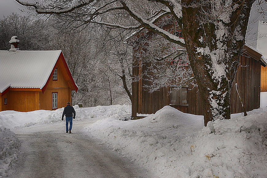 Man Walking Down Snowy Path Between Wooden Houses