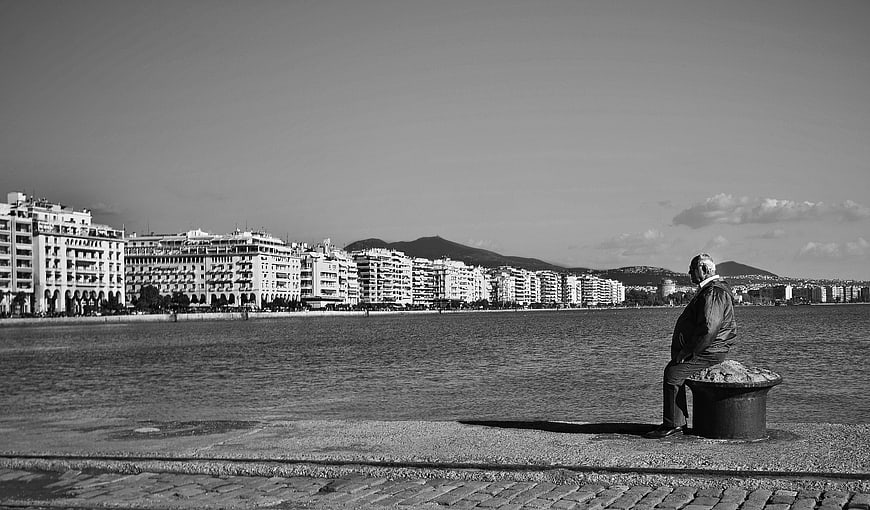 Elderly man sitting alone on seaside promenade in black and white
