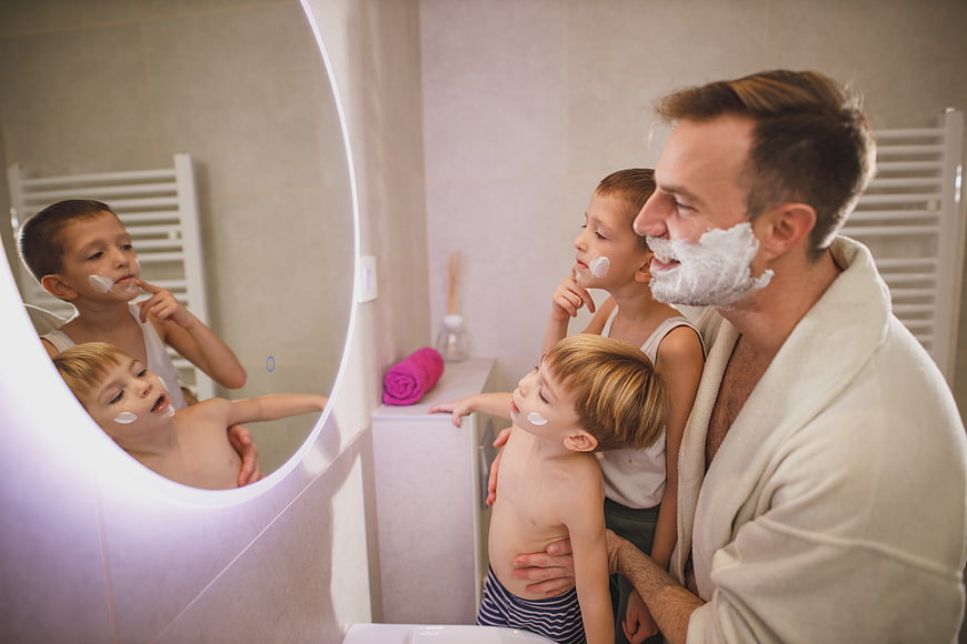 Father and sons shaving together in bathroom mirror