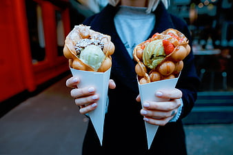 Hands holding two bubble waffle cones with ice cream and toppings