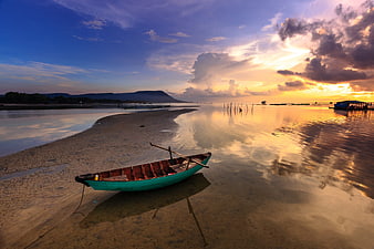 Traditional wooden boat on sandy beach at sunset