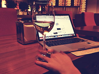 Woman's hand holding wine glass near laptop in restaurant