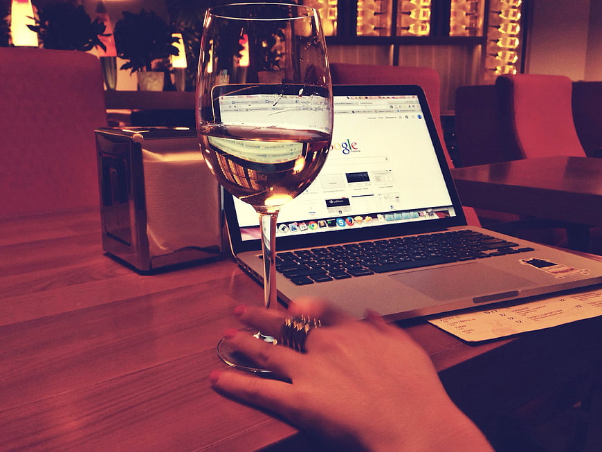 Woman's hand holding wine glass near laptop in restaurant