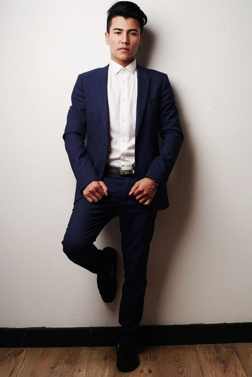 Handsome Asian Man in Blue Suit Leaning Against White Wall