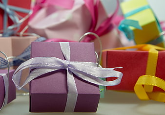 Close-up of purple gift box with white ribbon and colorful presents