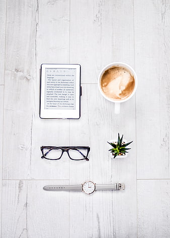 Flat lay of e-reader, coffee, glasses, and watch on white wood