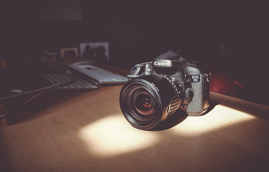 Canon DSLR Camera on Wooden Desk in Sunlight