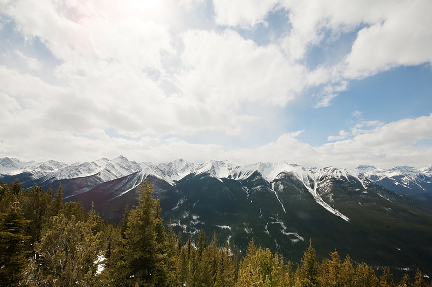 Snow-Capped Mountain Range with Pine Forest and Cloudy Sky