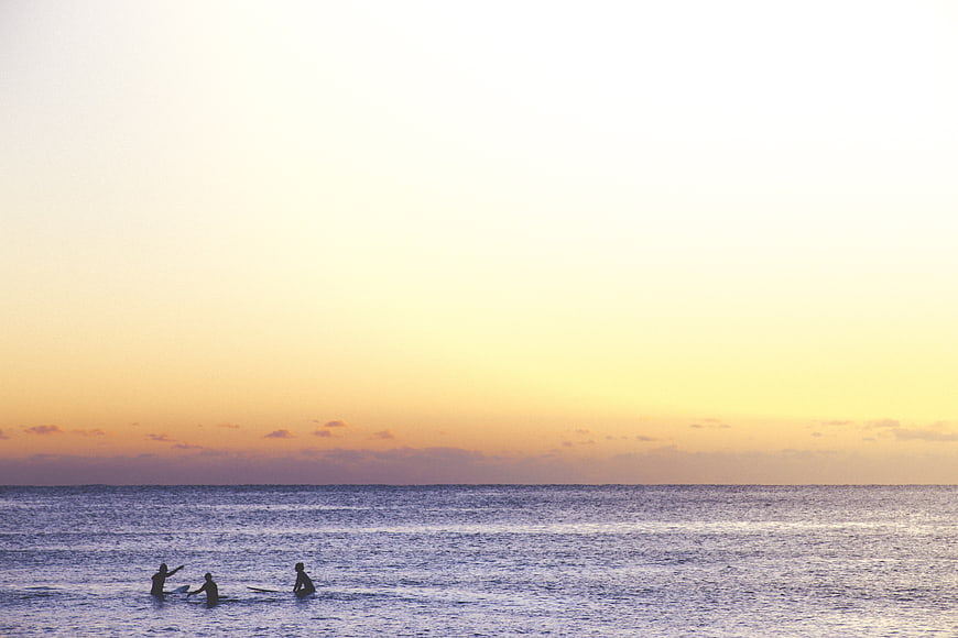 Surfers Silhouetted Against Golden Sunset Ocean Horizon
