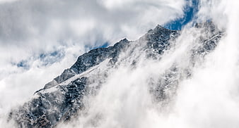 Snowy mountain peak emerging from thick white clouds