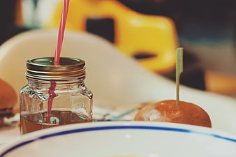 Close-up of iced tea in mason jar with pink straw and burger