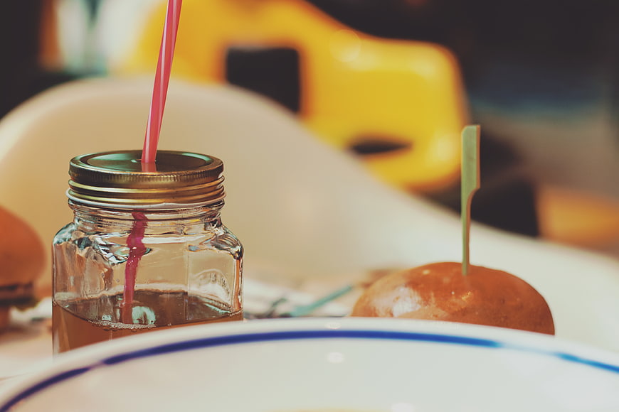 Close-up of iced tea in mason jar with pink straw and burger