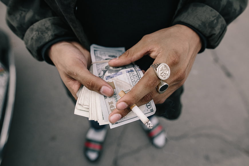 Man holding cash and cigarette with luxury rings