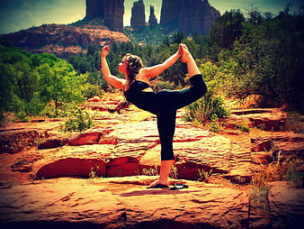Woman performing yoga pose on red rock in desert landscape