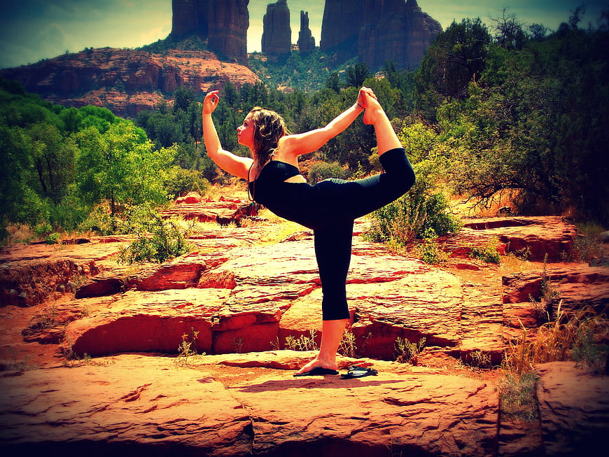 Woman performing yoga pose on red rock in desert landscape