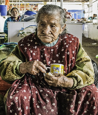 Elderly woman eating and drinking in a bustling market stall
