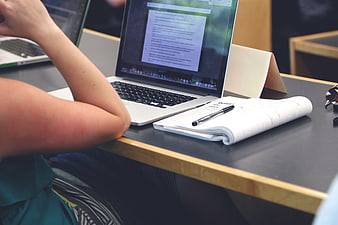 Person working on laptop with notebook and pen on desk