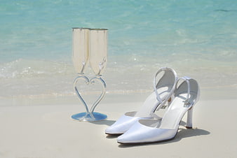 White bridal heels and heart-shaped champagne flutes on a tropical beach