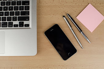Flat lay of laptop, smartphone, pens, and pink sticky notes on wooden desk