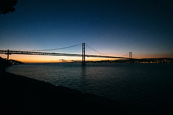 Silhouette of suspension bridge over water at twilight