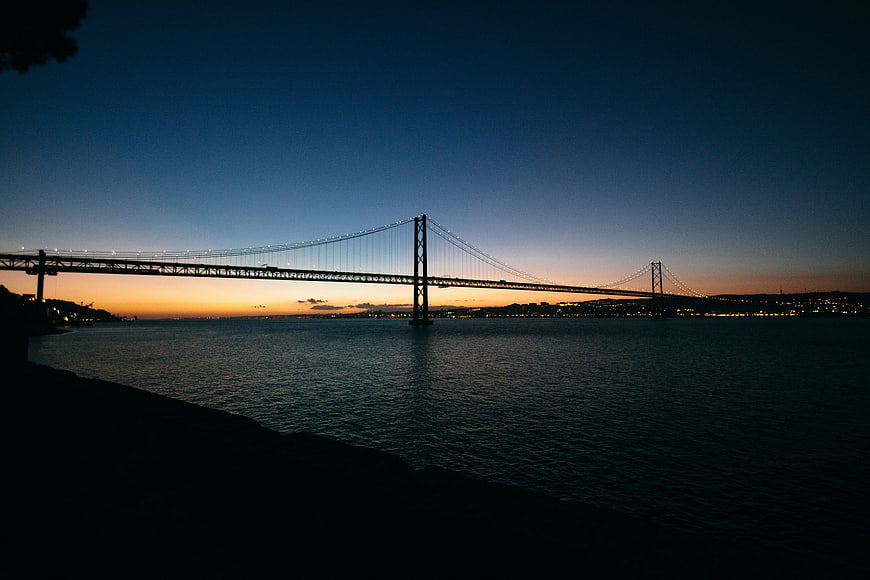 Silhouette of suspension bridge over water at twilight