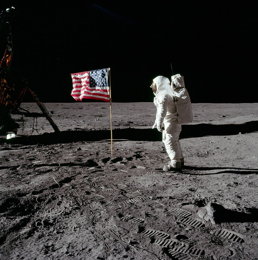 Astronaut standing next to American flag on the moon surface