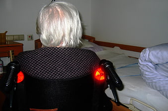 Senior woman with grey hair sitting in wheelchair facing bed