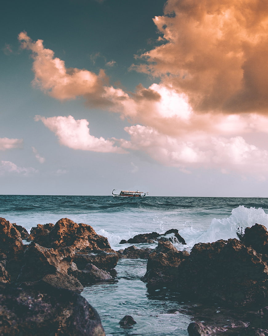 Traditional boat on ocean with dramatic sunset clouds and rocky shore