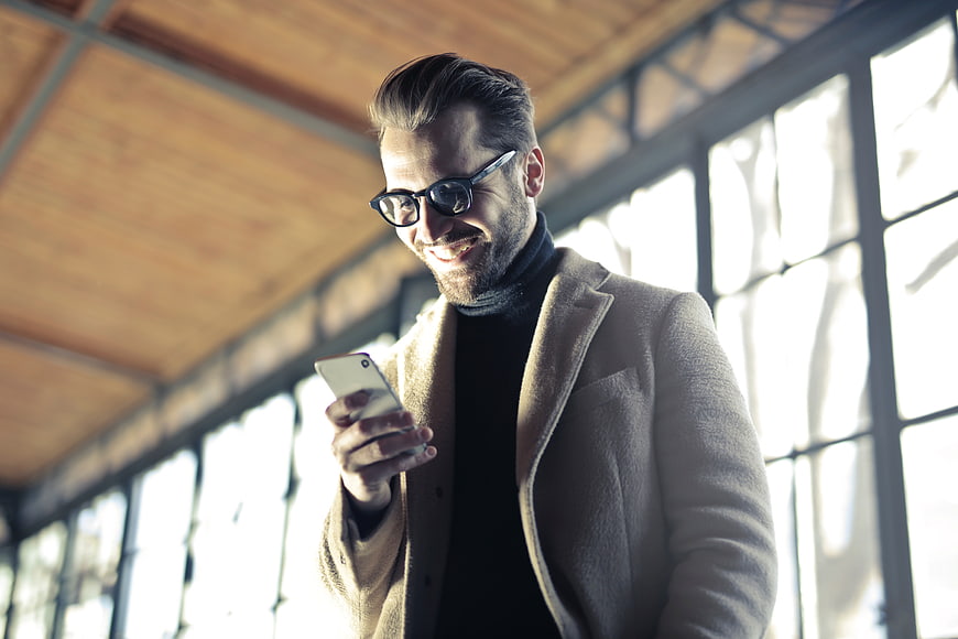 Smiling man with glasses using smartphone in modern office