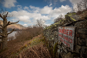 Rusty Danger Sign on Old Stone Wall in Rural Landscape