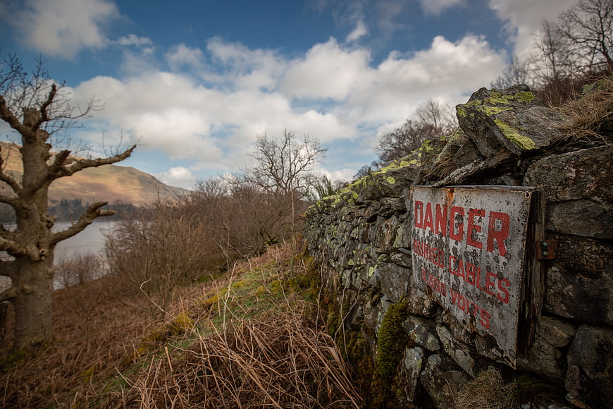 Rusty Danger Sign on Old Stone Wall in Rural Landscape