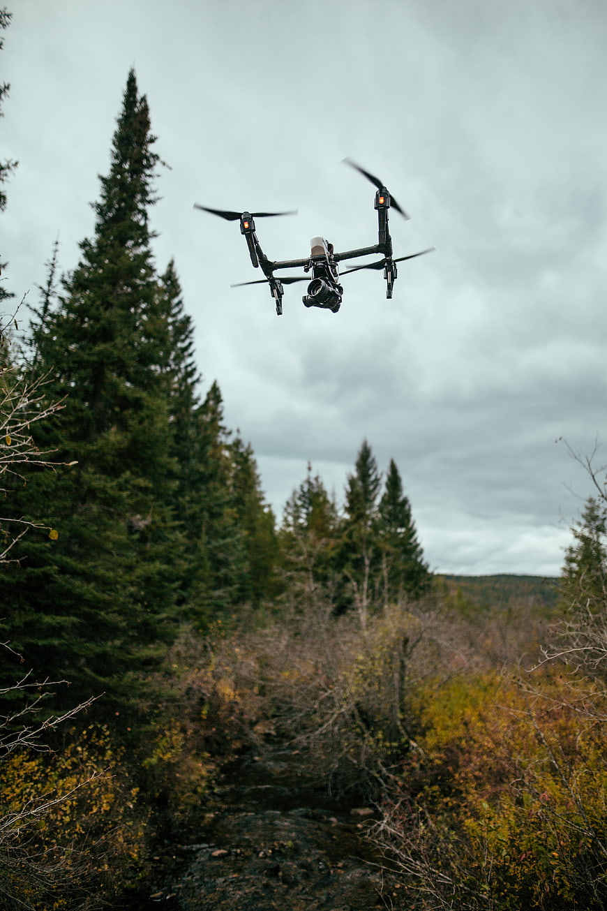 Professional drone with camera flying over autumn forest stream