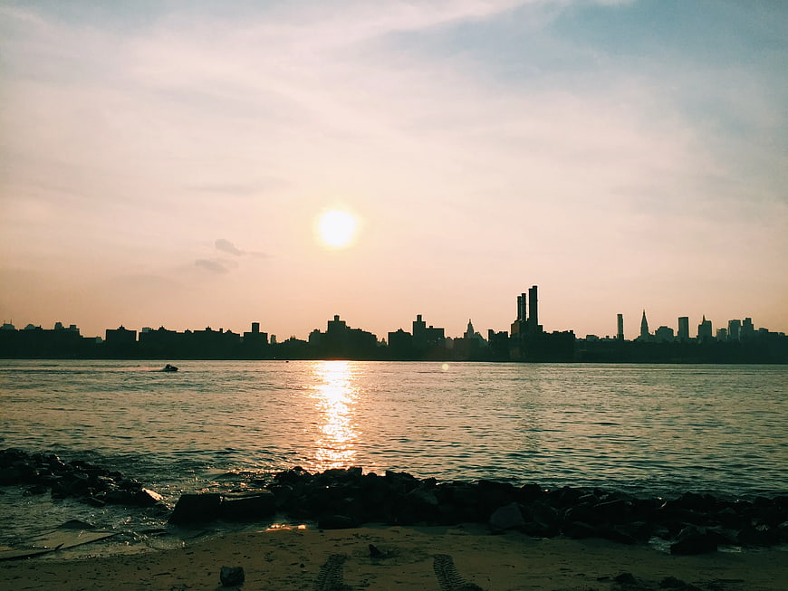 Sunset Silhouette of City Skyline Over Water and Beach