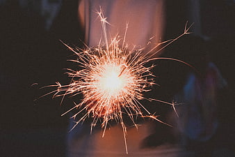 Close-up of a glowing sparkler with bright orange sparks against a dark background