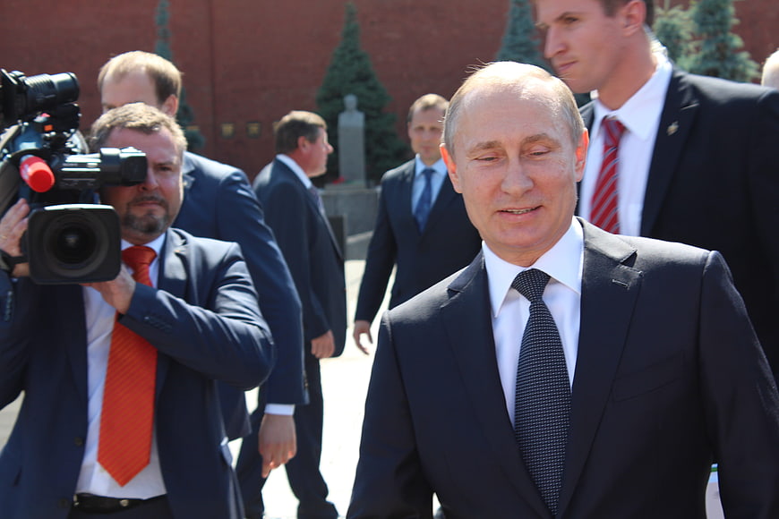 Vladimir Putin walking outdoors with press and security