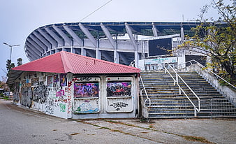 Graffiti-covered kiosk in front of large stadium
