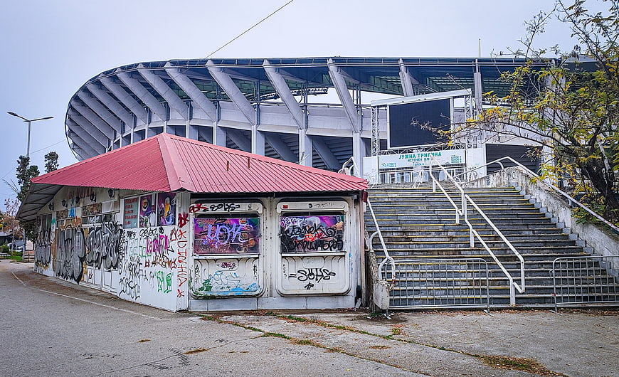 Graffiti-covered kiosk in front of large stadium