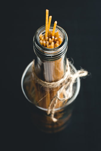 Uncooked spaghetti in a glass bottle on black background