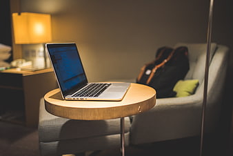 Laptop on wooden table in hotel room with lamp and sofa