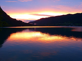 Serene sunset reflection on calm lake surrounded by mountains