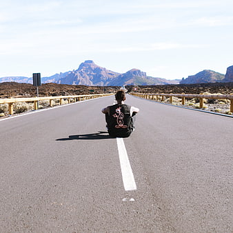 Man sitting on empty road with mountains in background