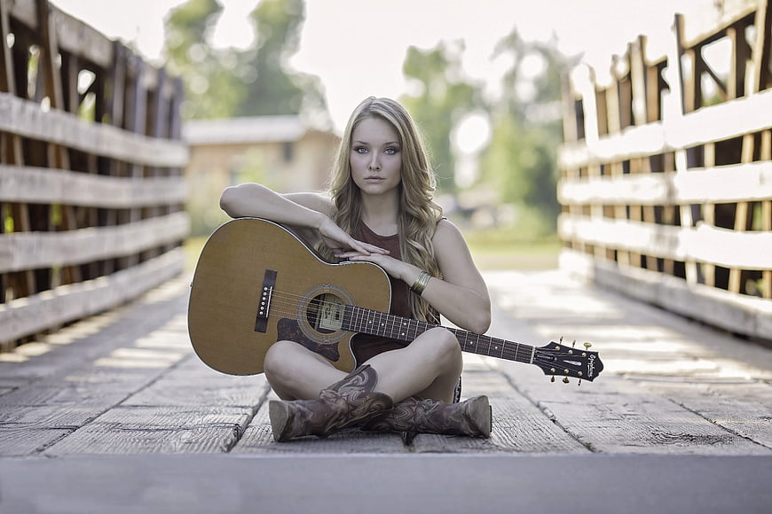Young Woman with Acoustic Guitar on Wooden Bridge