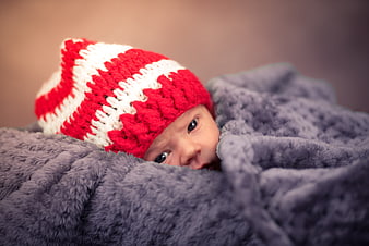 Newborn baby girl wearing red and white knit hat wrapped in gray blanket
