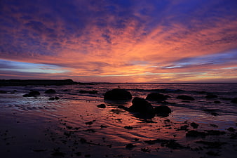 Vibrant Sunset Over Rocky Beach with Silhouetted Stones