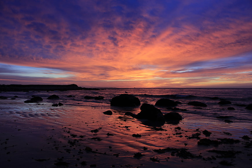 Vibrant Sunset Over Rocky Beach with Silhouetted Stones